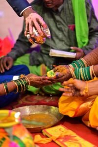 Close-up of a traditional Indian wedding ritual with henna-adorned hands and vibrant attire.